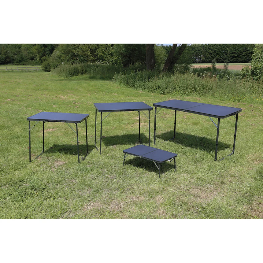 Four Quest camping tables on grass, with the low Witney table at the front for size comparison
